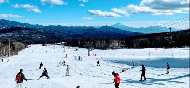 Skiers on a wide beginner slope with Mount Fuji beyond